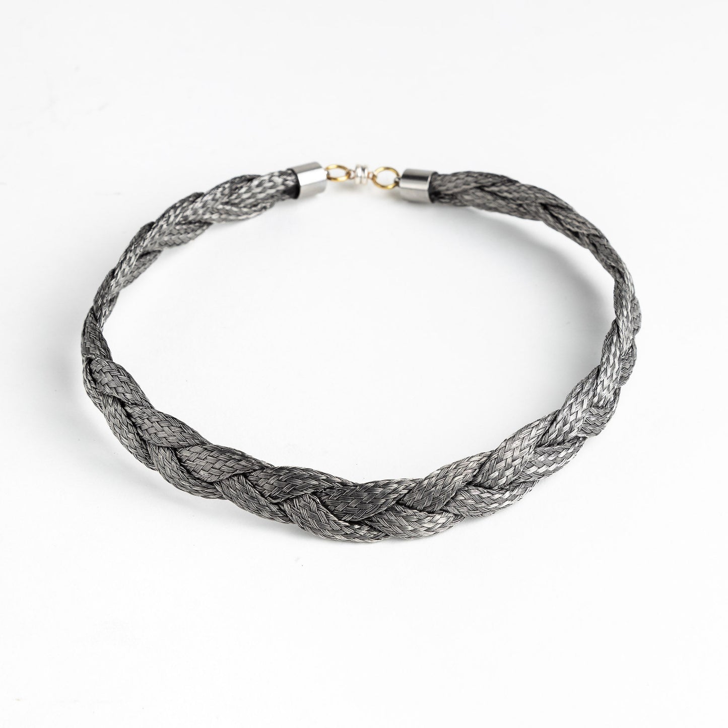 Braided stainless steel necklace with gold clasp on a white background, forming a loose circle.