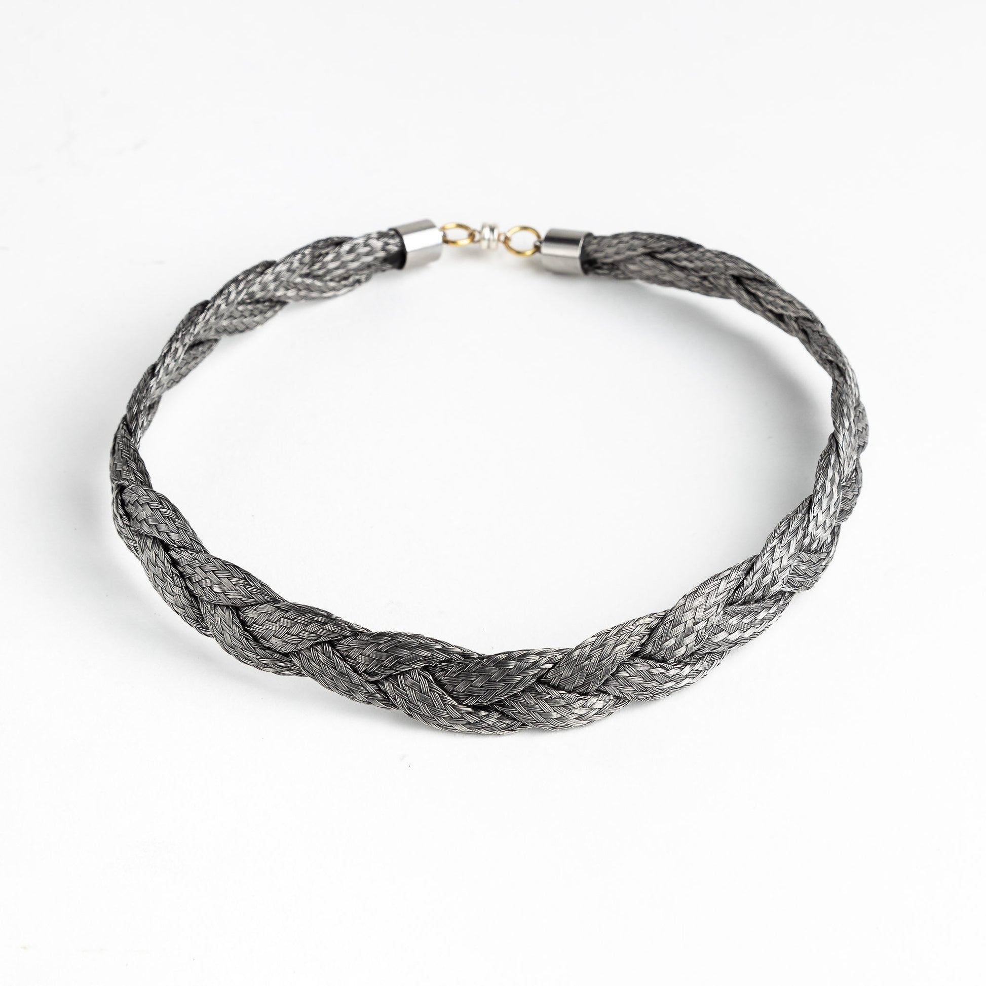 Braided stainless steel necklace with gold clasp on a white background, forming a loose circle.