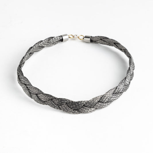 Braided stainless steel necklace with gold clasp on a white background, forming a loose circle.