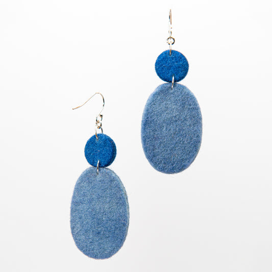 Two blue felt earrings hang from silver hooks. Each earring has a smaller circular piece above a larger oval piece.
